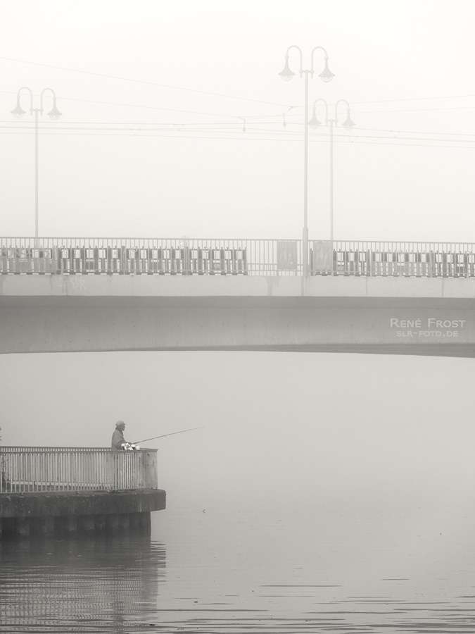 Der Angler unter der im Nebel schwebenden Brücke